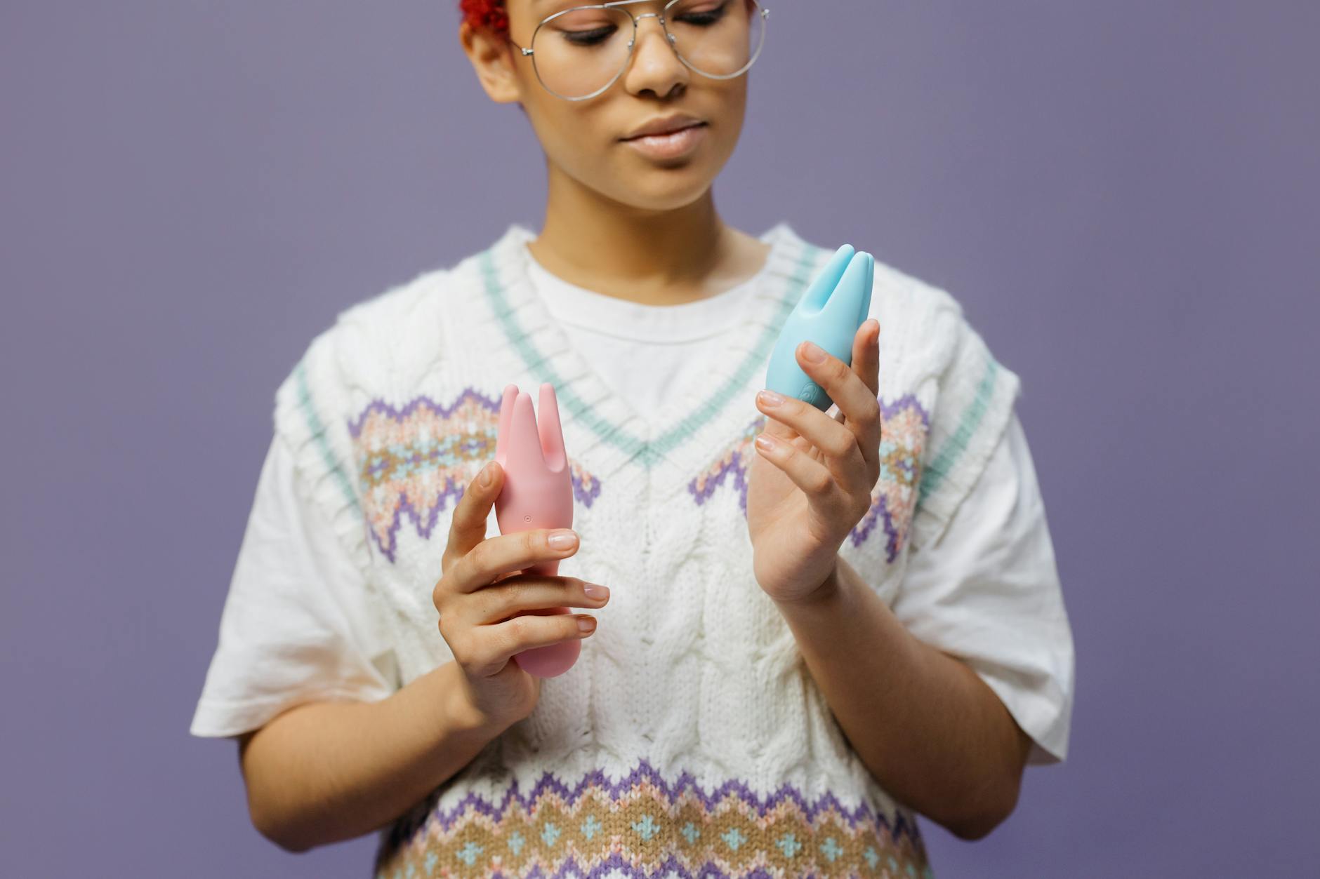 A hand reaching over a variety of colorful sex toys arranged on a table.